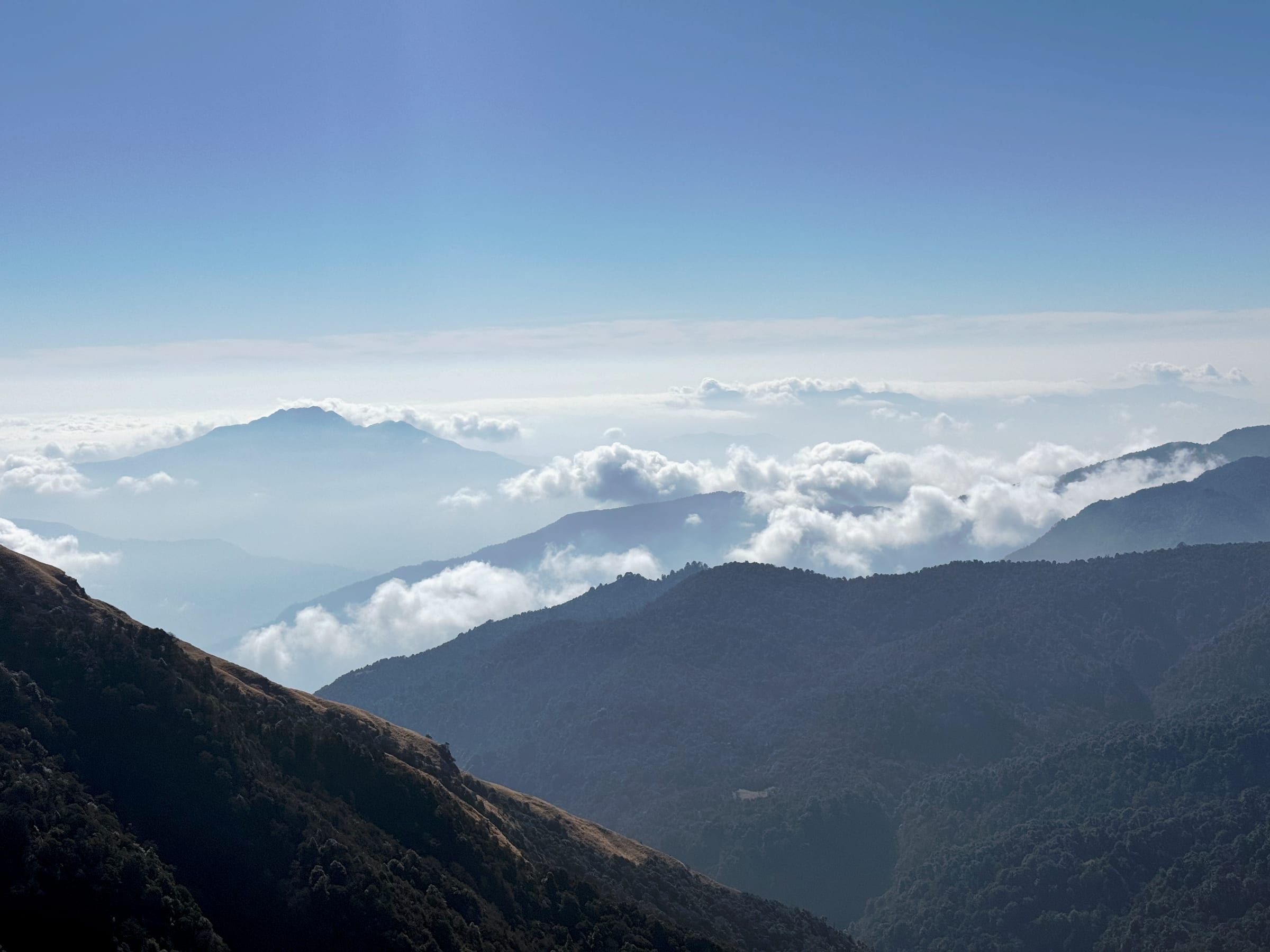 Hazy mountain silhouettes rising above a thick sea of cloud, seen from high altitude