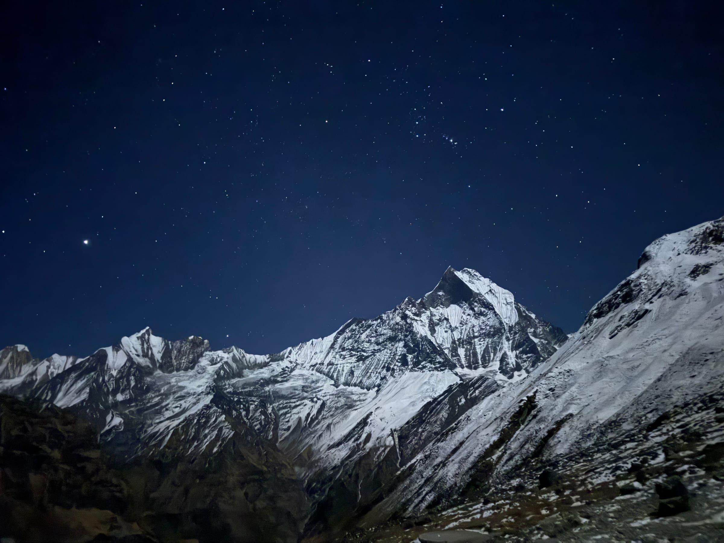 A snow peak glowing faintly under a darkening evening sky filling with stars