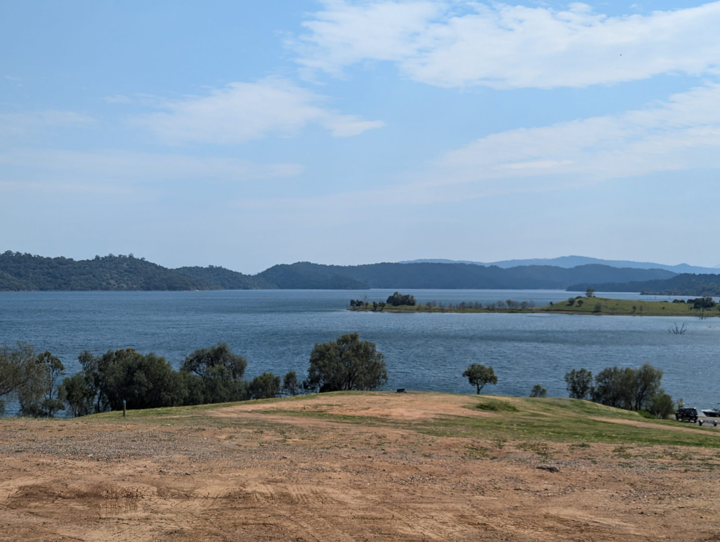 A wide view of Lake Glenbawn with small islands and rolling hills in the distance, dry ground in the foreground