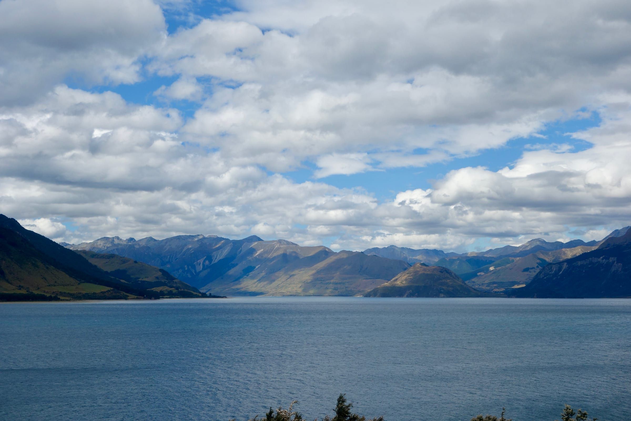 A wide lake framed by layered mountain ranges under a heavy sky of scattered cloud