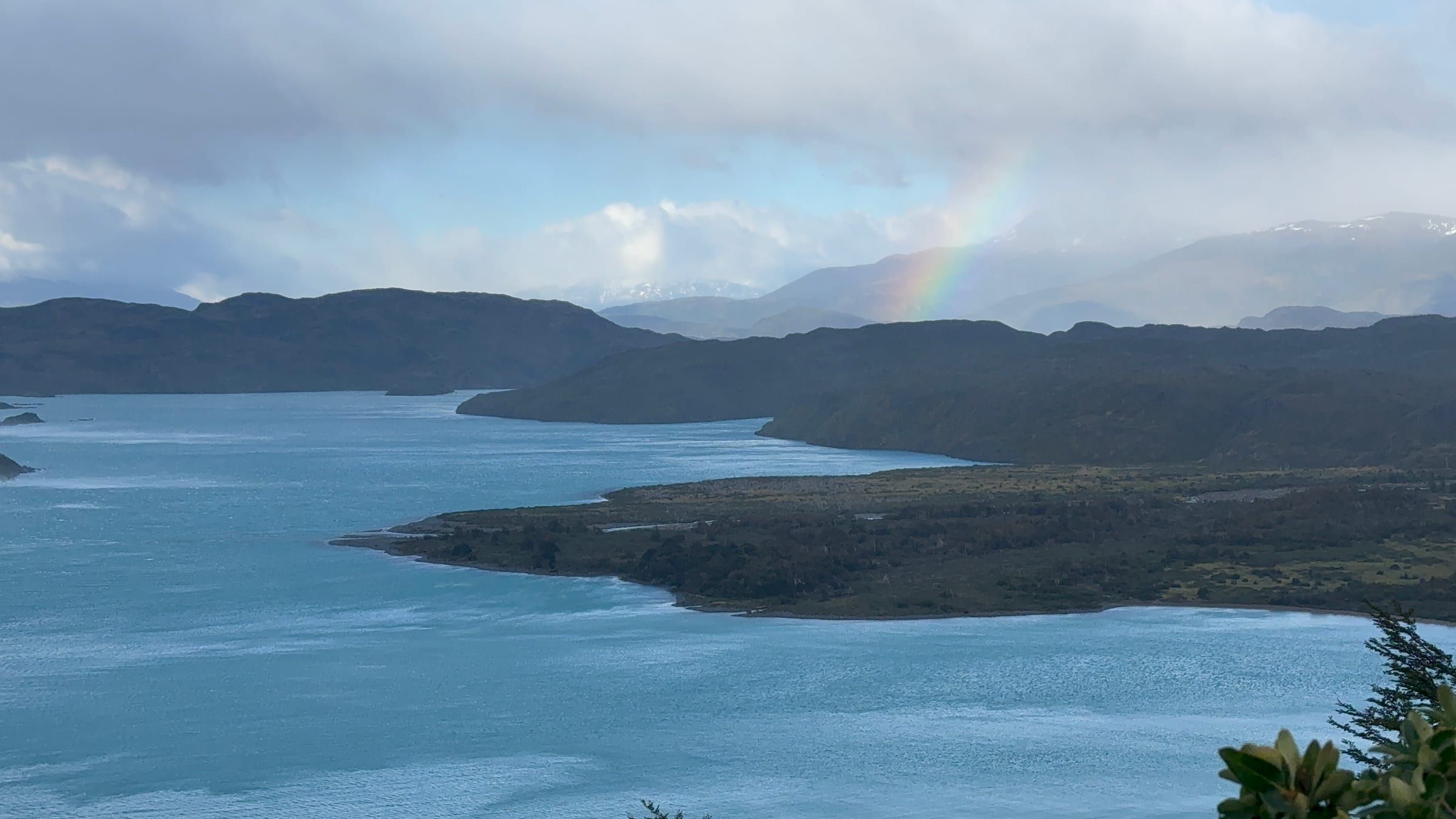 A faint rainbow over a fjord, dark mountain ridgelines under stormy clouds