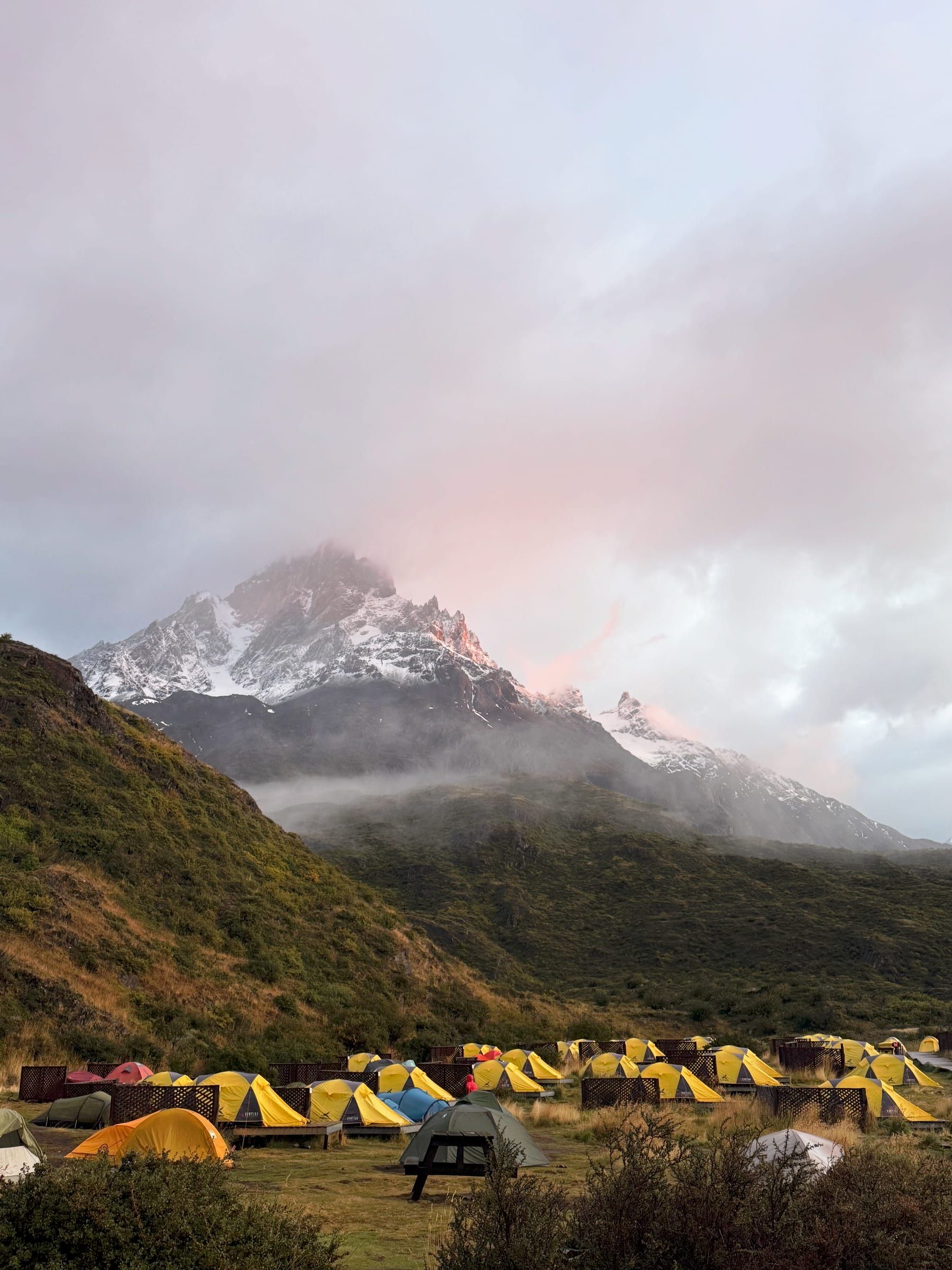 Rows of yellow tents at a trekking camp, misty mountain peak behind