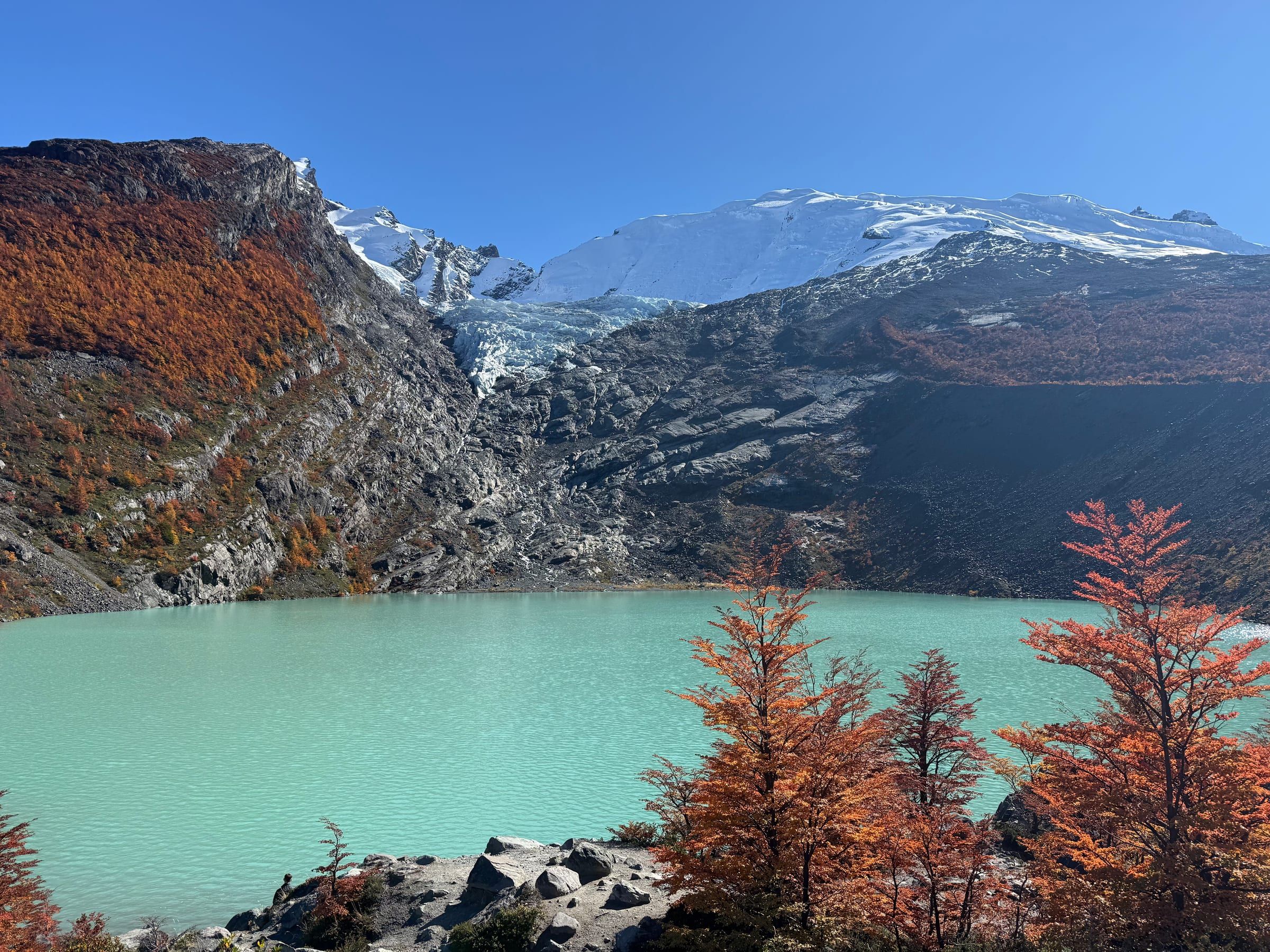 Turquoise glacial lake with a hanging glacier and autumn-red trees in the foreground