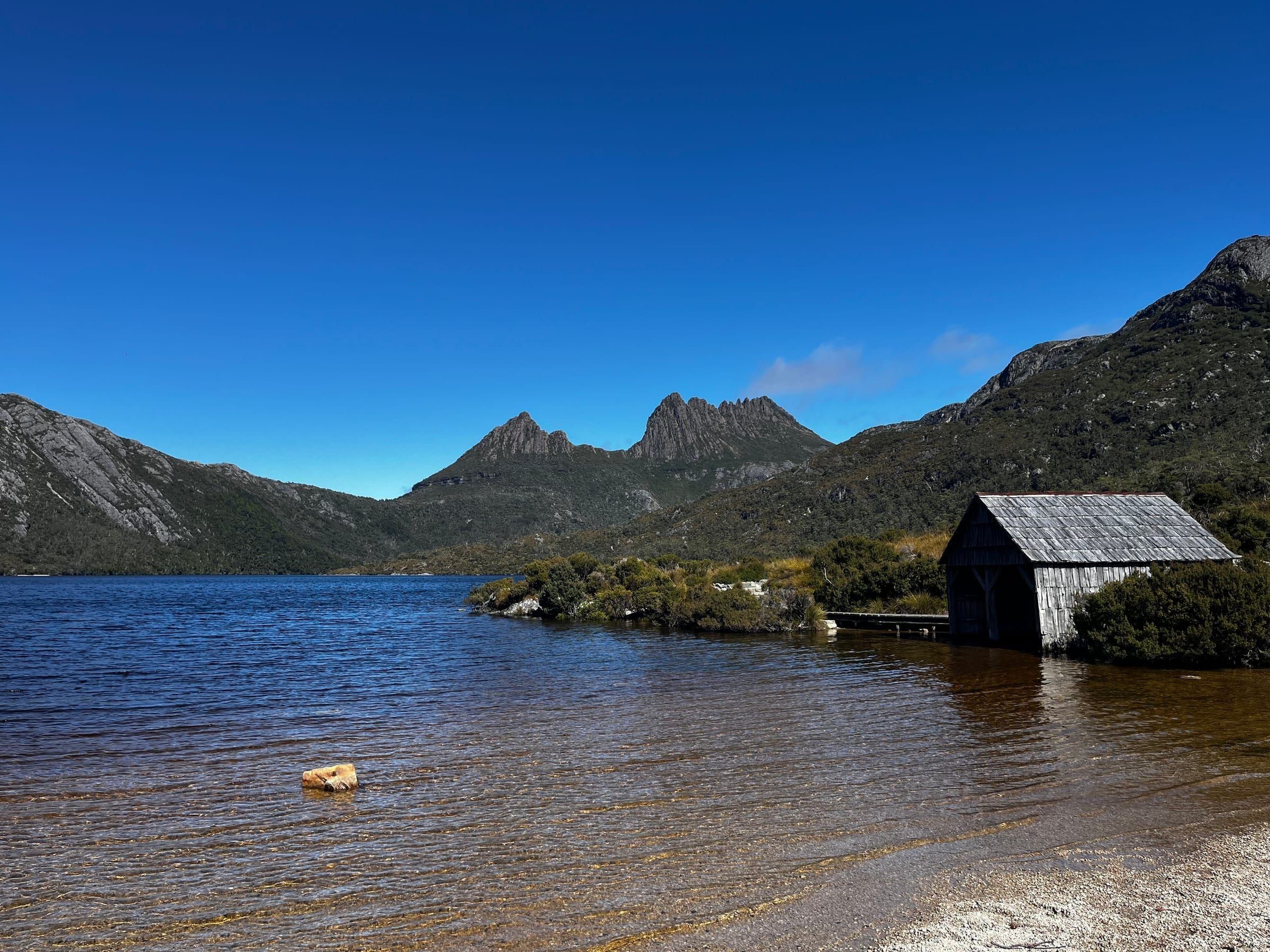 The iconic Dove Lake boat shed, weathered timber, with Cradle Mountain's peaks rising behind it