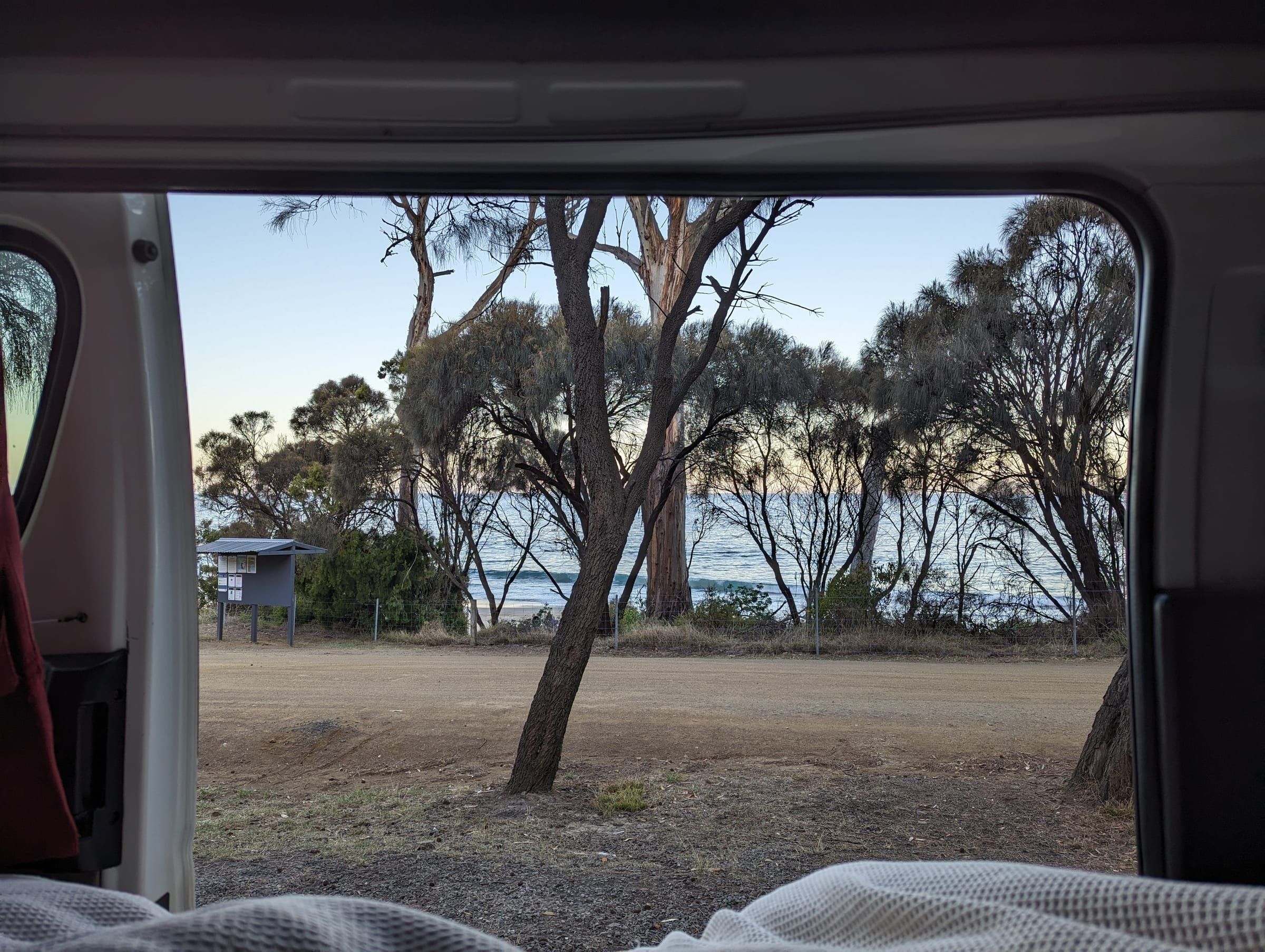 View from inside the open van doors straight out to the ocean through a screen of trees