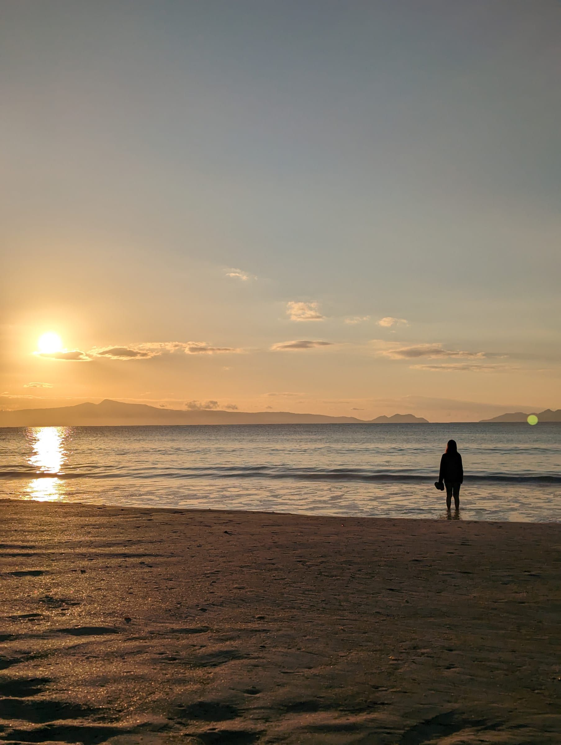 A silhouetted figure standing at the water's edge as the sun rises over the sea