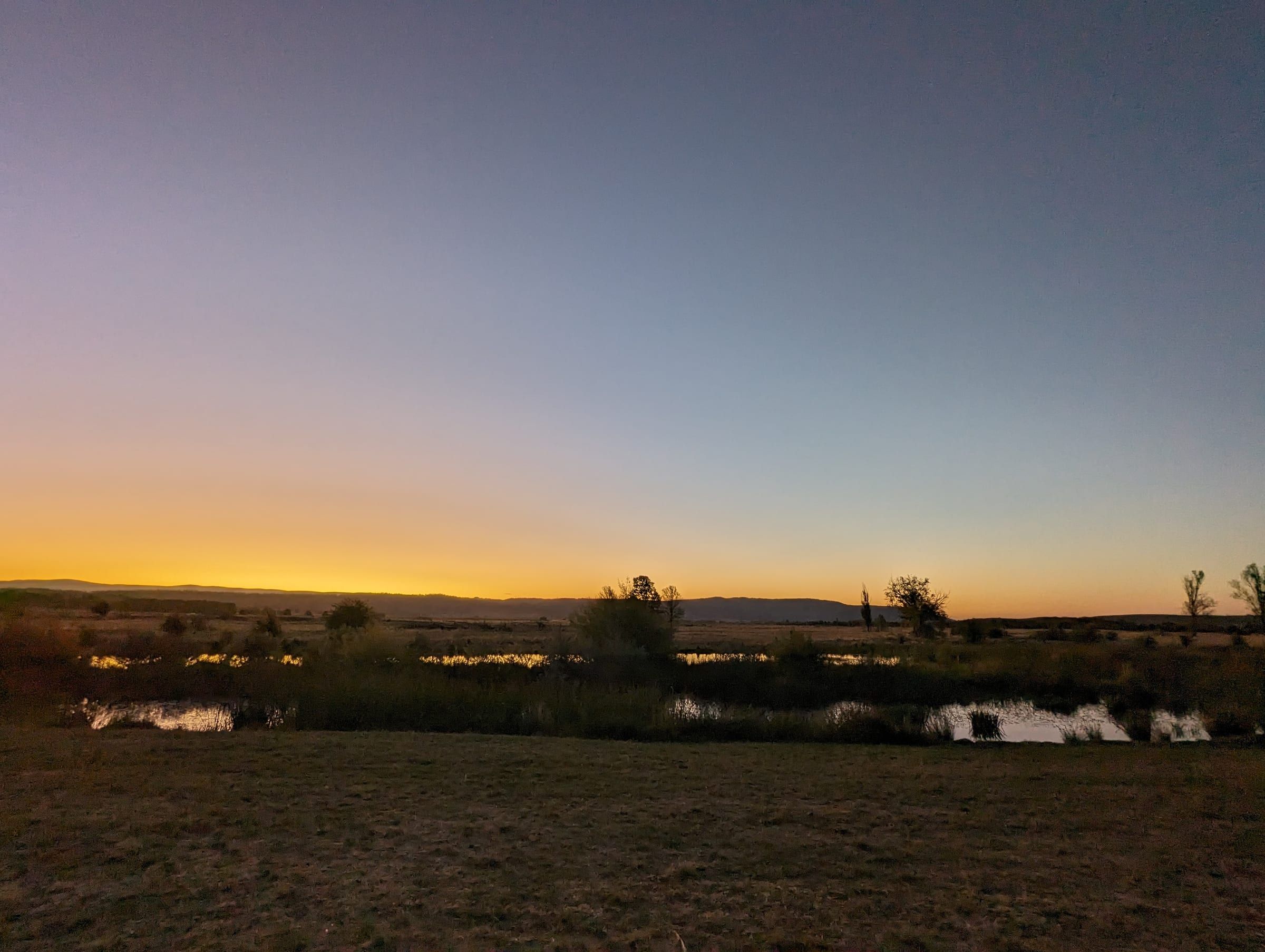Open countryside at dusk, golden sunset light over wetlands and distant hills