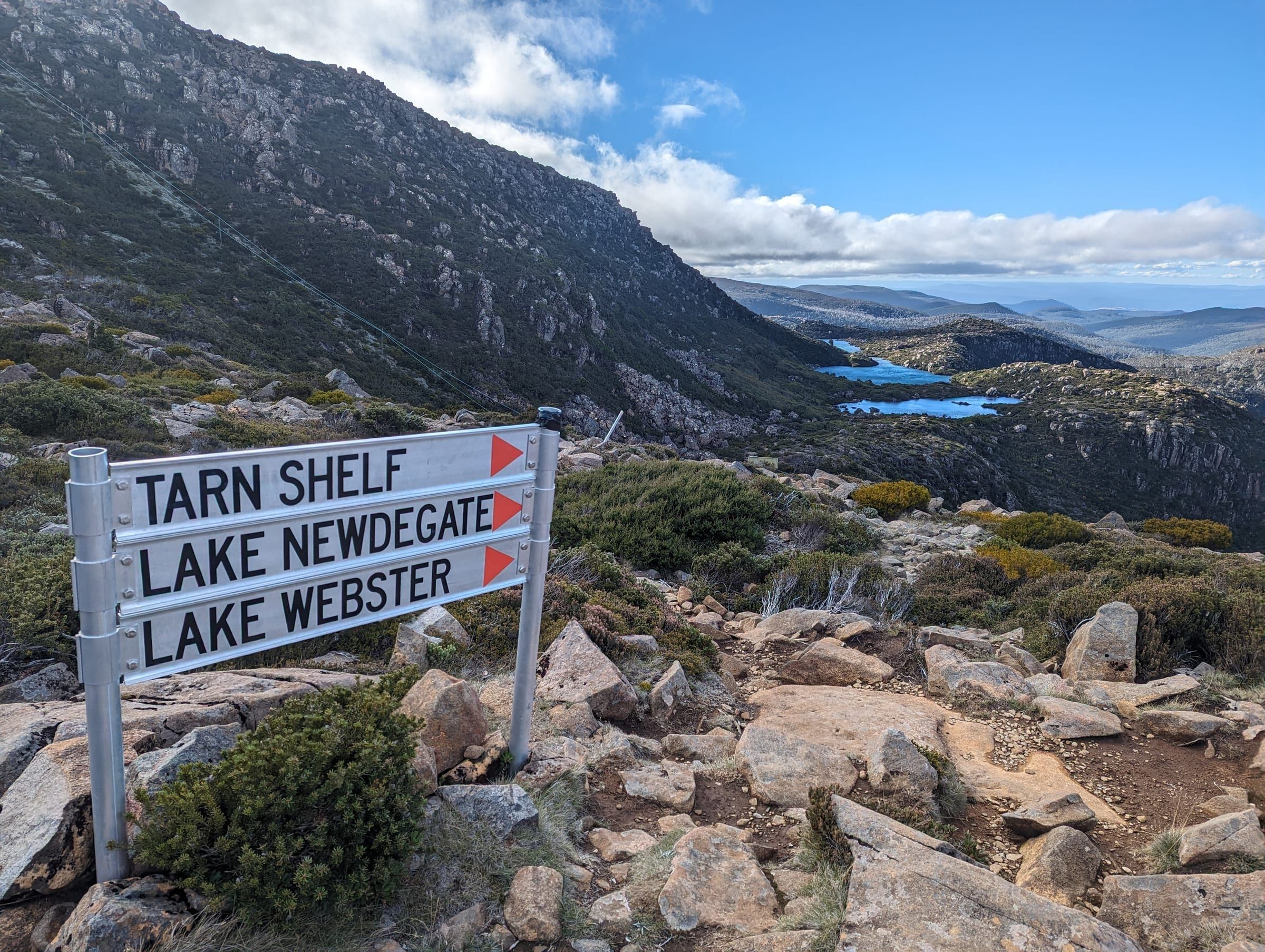 The Tarn Shelf trail sign, with vivid blue alpine tarns visible in the valley below