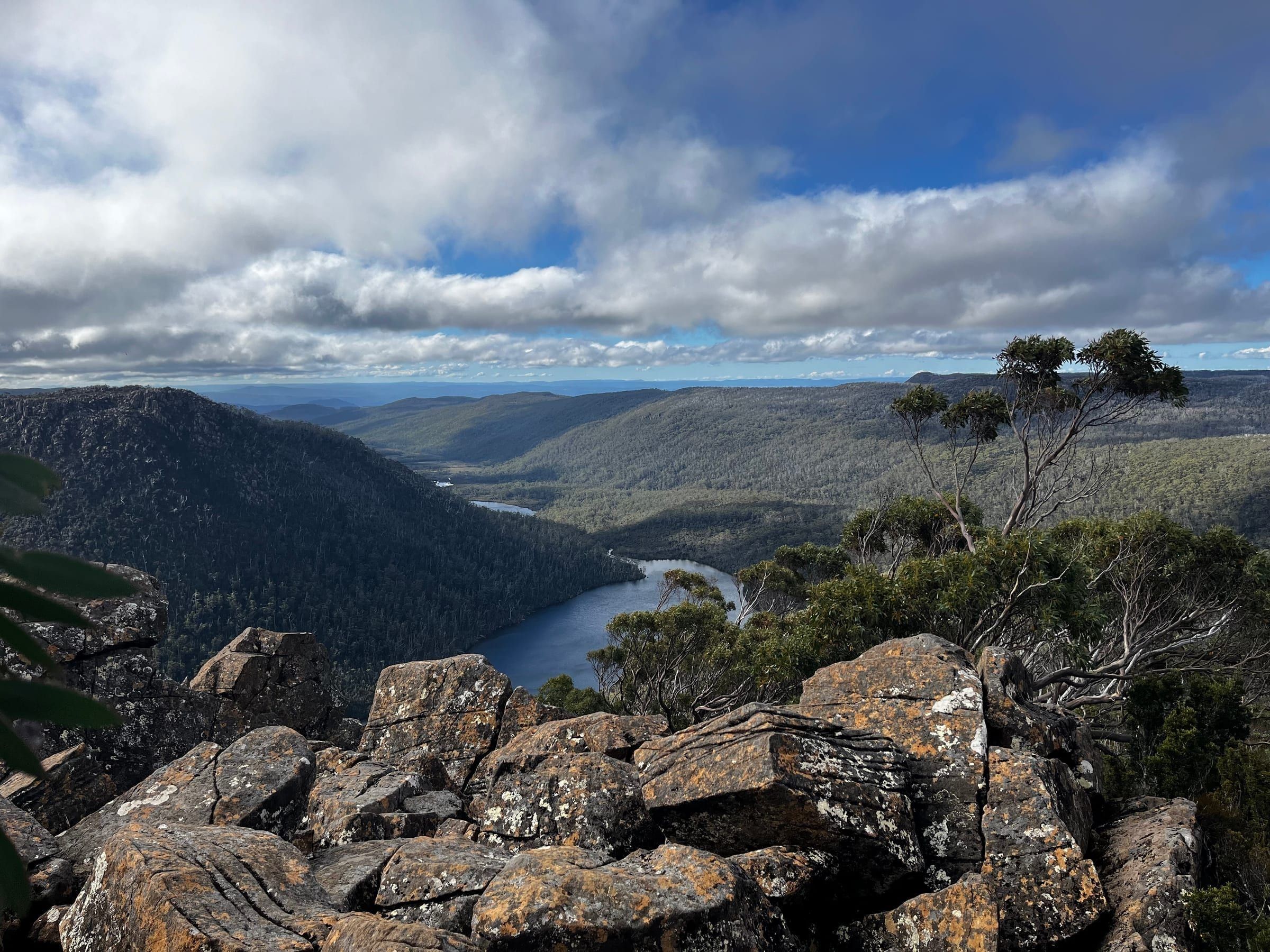 A wide valley view with a river winding through forested hills, seen from a rocky lookout
