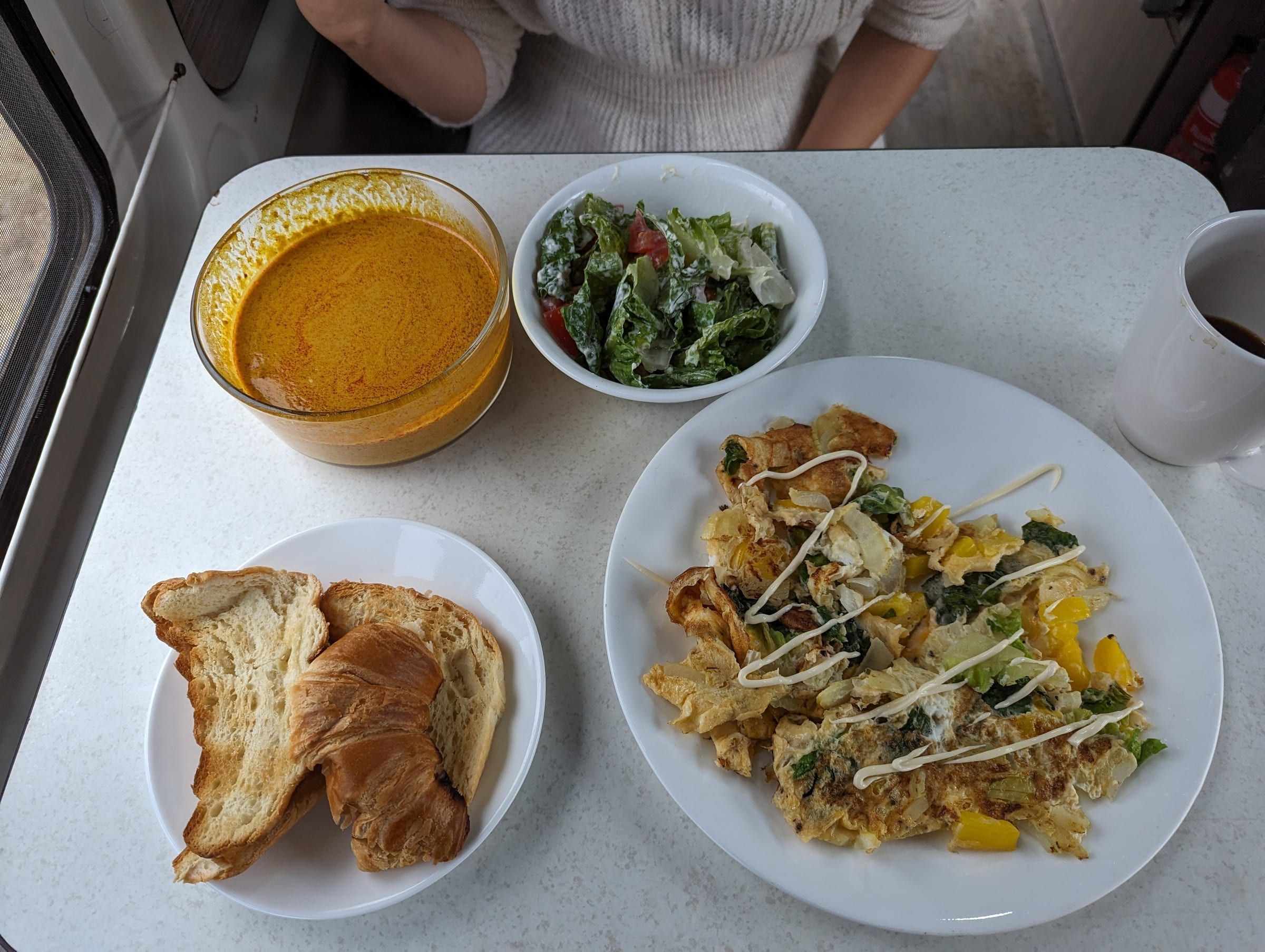 A hearty van breakfast: pumpkin soup, a caesar-style salad, toast and croissant, and a vegetable scramble, with coffee